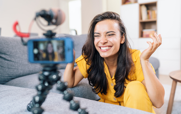 Woman in yellow sweater laughing into camera on tripod