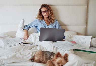 Shot of a young woman using a laptop while working in bed