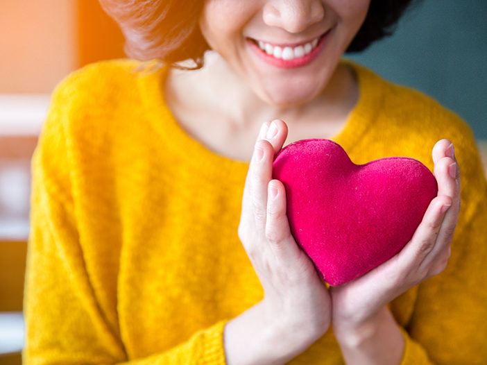 Woman hands in yellow sweater holding pink heart.