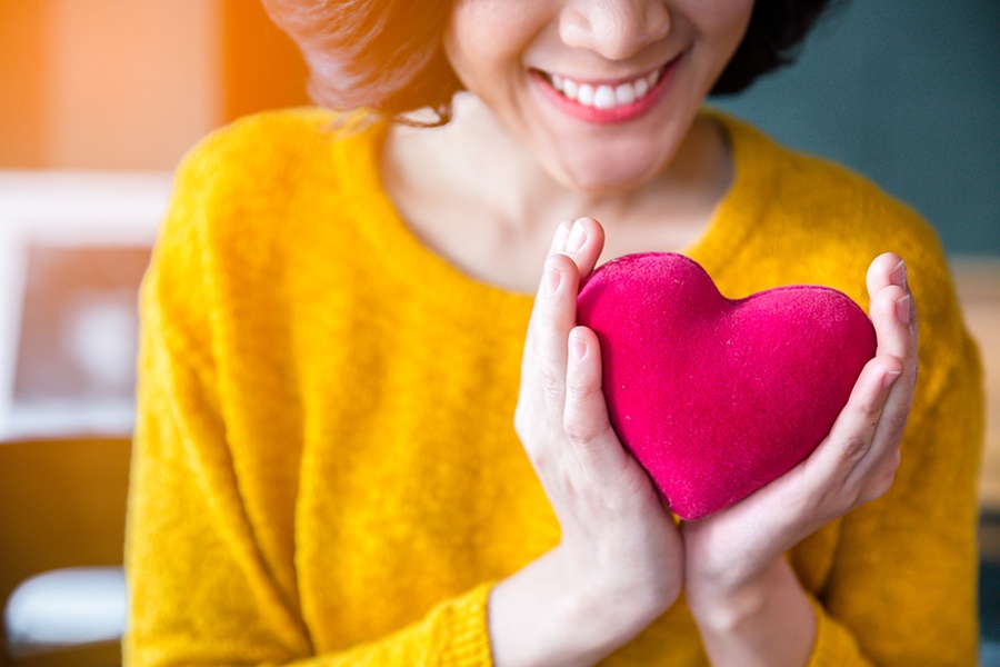 Woman smiling in a yellow knit sweater holding a felt heart.