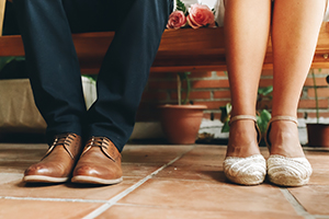 Shoes of groom and bride and her small wedding bouquet of pink roses sitting and waiting in a wooden bench. Wedding day concept.