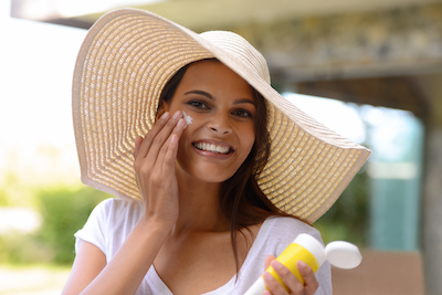 Woman in a sun hat applying sunscreen