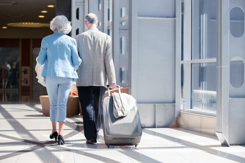 A senior couple walking together in an airport pulling rolling luggage behind them