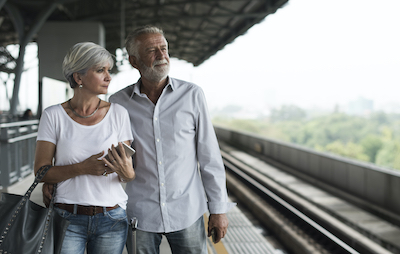A senior couple standing at a train station platform looking off into the city below