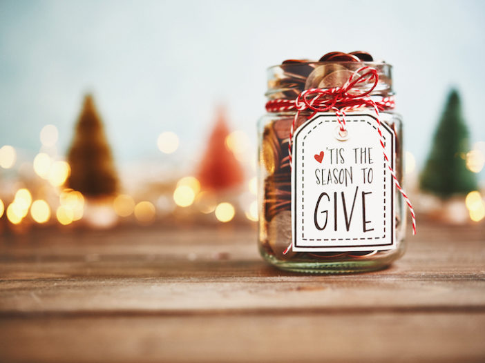 A jar full of pennies with a handwritten label that reads "'Tis the season to give" tied on with festive red and white string