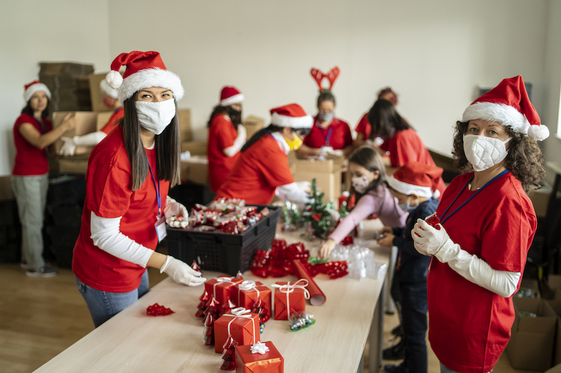 Volunteers wearing red shirts and Santa hats wrapping gifts together