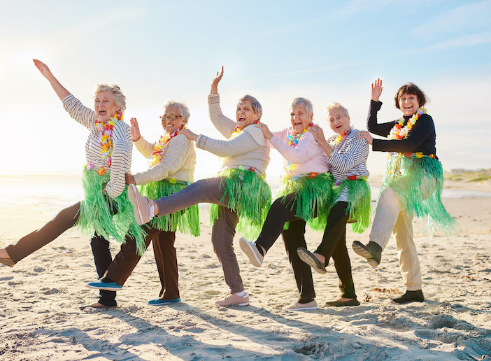 Senior ladies in grass skirts forming a conga line on a beach