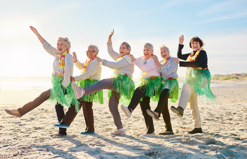Senior ladies in grass skirts laughing and forming a conga line on the beach