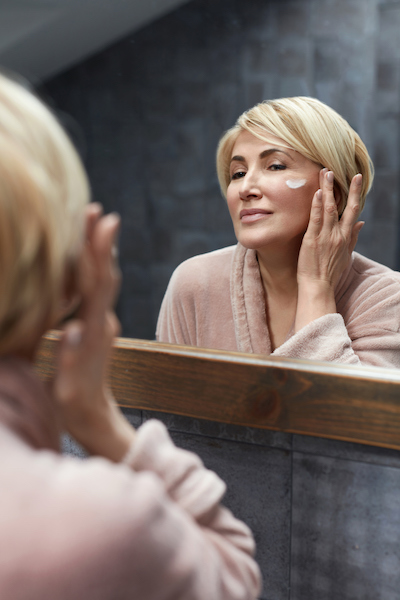 A woman looking in the mirror applying creams to her face