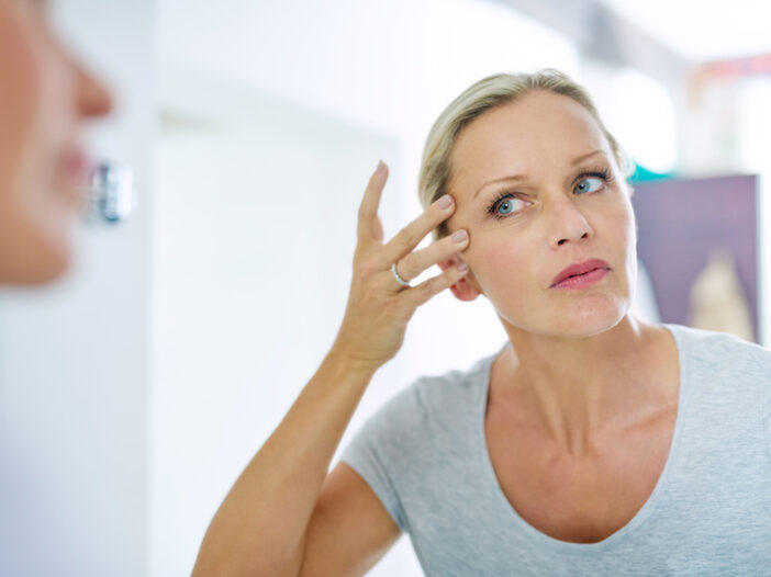 Woman looking at facial wrinkles in mirror