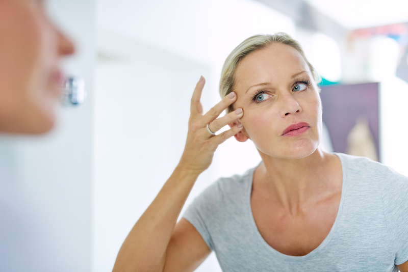 A woman looks at wrinkles around her eyes in a mirror