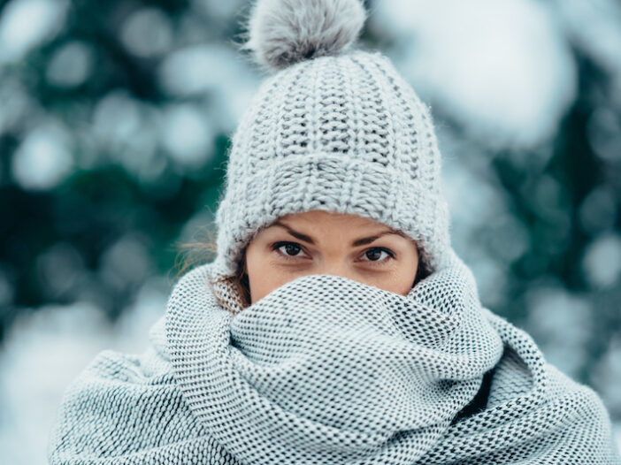 Woman in white knit Winter cap covers her face with a white scarf