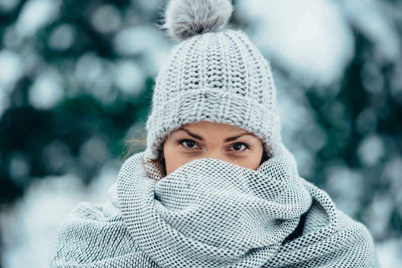 Woman in white knit Winter cap covers her face with a white scarf to protect from cold weather